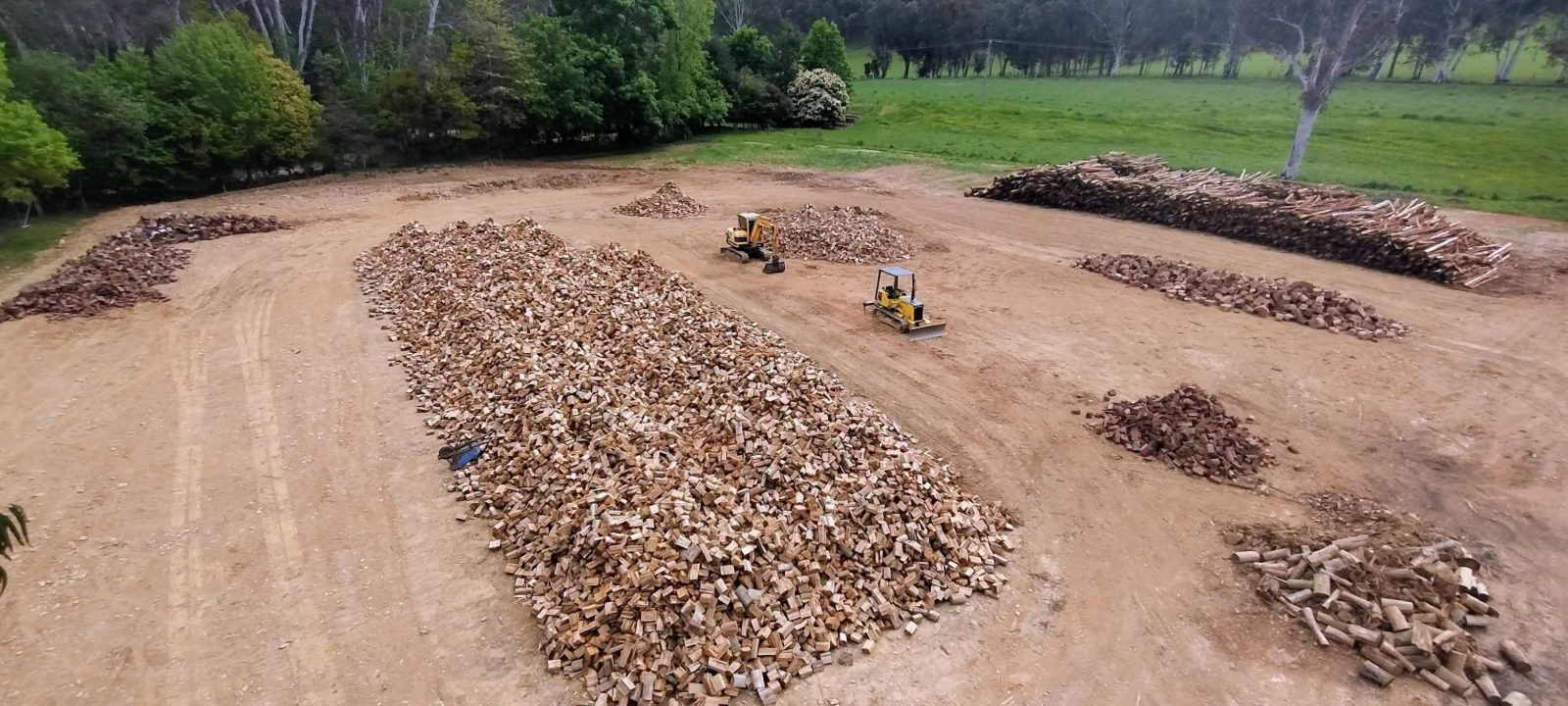 Drone shot of the Skyline Firewood yard in Bright: long rows of split firewood, a loader and a dozer